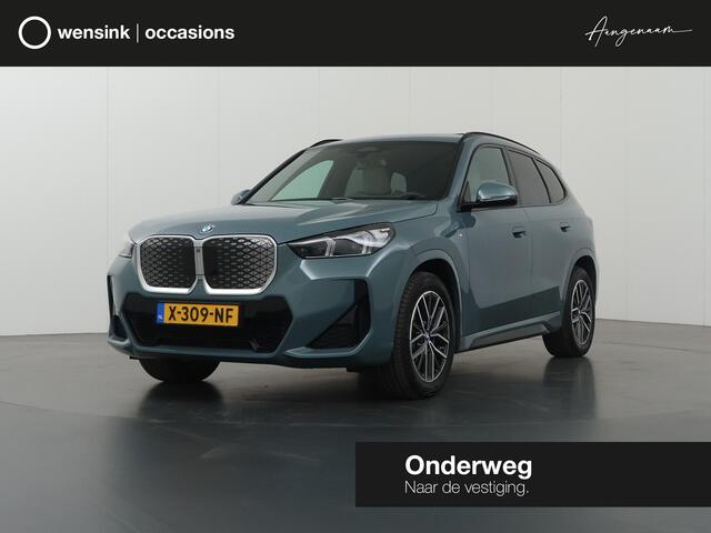 BMW iX1 eDrive20 67 kWh M-Pakket | SOH 98% | Panormadak | Sportstoelen | Curved Display | Harman/Kardon | Camera | Apple CarPlay/Android Auto | Ele.verstelbare stoelen + Geheugen | Ele. kofferdeksel |